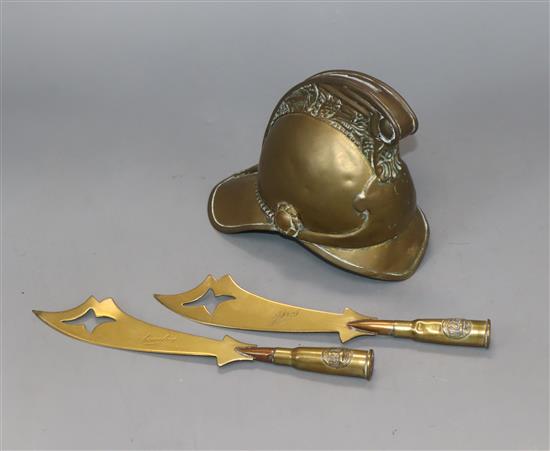 An early 20th century model brass firemans helmet money box, two trench art paperknives and a shell case